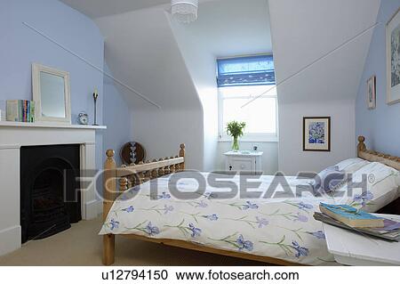 Blue iris-patterned bedlinen on bed in pastel blue attic bedroom with white fireplace View Large Photo Image Stock Image - Blue iris-patterned bedlinen on bed in pastel blue attic bedroom with white fireplace. Fotosearch