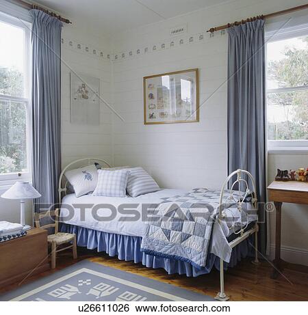 Stock Photograph - Blue patchwork quilt and white linen on white bed in blue+white themed bedroom. Fotosearch