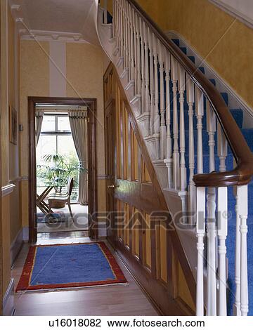 Stock Image - Blue rug on floor in townhouse hall with under-stair cupboards and painted white bannisters. Fotosearch