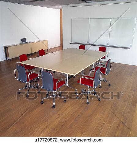 Stock Image - Blue+red swivel chairs and empty boardroom table in modern office with wooden flooring. Fotosearch