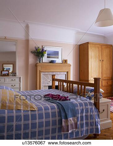 Stock Photo - Blue+white checked bed-cover on wooden bed in economy style bedroom. Fotosearch