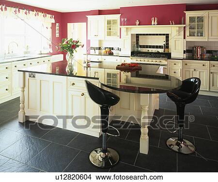 Picture - Bomba stools at breakfast bar in red kitchen with cream units and slate floor tiles. Fotosearch