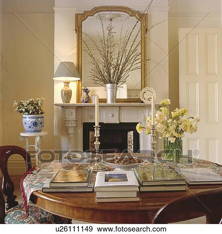 Books and fresh flowers in vase on antique table in neutral dining room with gilt mirror above fireplace View Large Photo Image Stock Photo - Books and fresh flowers in vase on antique table in neutral dining room with gilt mirror above fireplace. Fotosearch