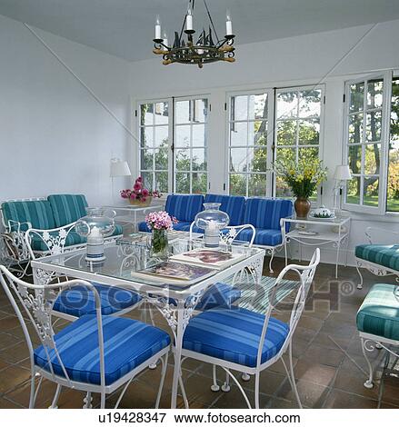 Bright blue cushions on white metal chairs at glass and metal table in white dining room extension View Large Photo Image Stock Photo - Bright blue cushions on white metal chairs at glass and metal table in white dining room extension. Fotosearch