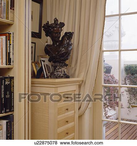 Bronze bust on narrow pale wood chest-of-drawers beside window with cream curtain View Large Photo Image Stock Photo - Bronze bust on narrow pale wood chest-of-drawers beside window with cream curtain. Fotosearch