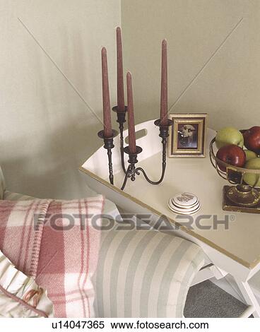 Stock Photography - Brown candles in metal candlestick on cream tray table beside striped sofa with pink and white checked cushion. Fotosearch