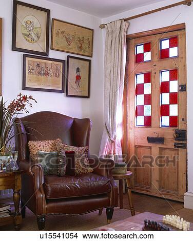 Picture - Brown leather armchair beside pine front door with stained-glass panel. Fotosearch