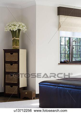 Bunch of cream faux orchids on narrow cupboard with storage baskets in modern white bedroom View Large Photo Image Stock Photograph - Bunch of cream faux orchids on narrow cupboard with storage baskets in modern white bedroom. Fotosearch