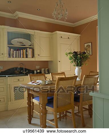 Stock Photo - Cane-back chairs and wooden table in traditional terracotta country kitchen with fitted cream cupboards. Fotosearch