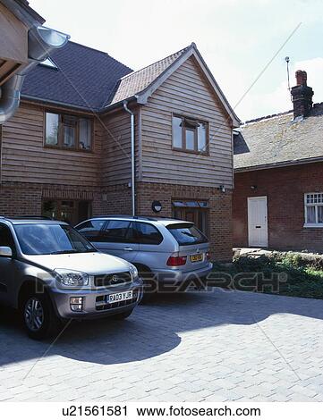 Stock Image - Cars on paved drive in front of timbered newbuild house. Fotosearch