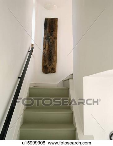 Stock Photography - Carved wood sculpture on staircase wall above modern grey painted wooden staircase. Fotosearch