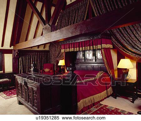 Carved wooden antique chest below carved bed with red bedcover and drapes in beamed country bedroom View Large Photo Image Stock Photography - Carved wooden antique chest below carved bed with red bedcover and drapes in beamed country bedroom. Fotosearch