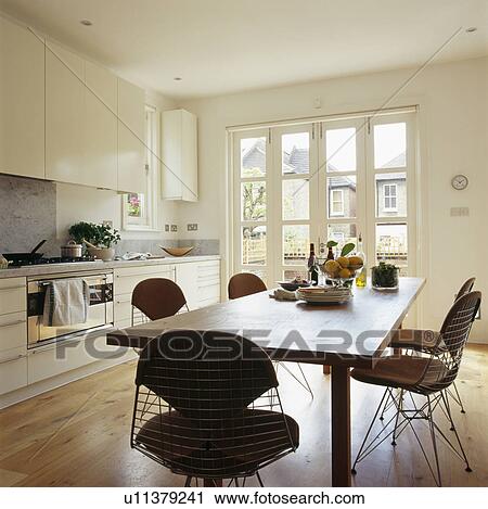 Stock Image - Charles Eames chairs with simple wooden table in large cream townhouse kitchen with wooden flooring. Fotosearch