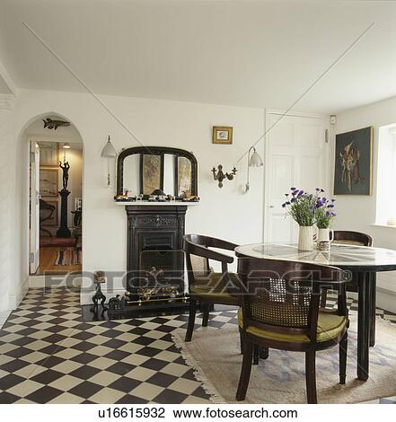 Stock Image - Chequerboard floor in white dining room with antique table and chairs. Fotosearch