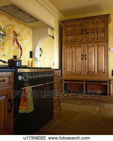 Chestnut-wood cupboard concealing fridge-freezer in yellow kitchen with black range oven and flagstone floor View Large Photo Image Stock Image - Chestnut-wood cupboard concealing fridge-freezer in yellow kitchen with black range oven and flagstone floor. Fotosearch