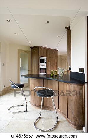 Stock Photo - Chrome and black leather stools at breakfast bar on walnut island unit in modern kitchen with limestone flooring. Fotosearch
