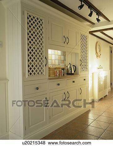 Stock Photo - Chrome kettle on inset worktop in large fitted cream kitchen cupboard. Fotosearch