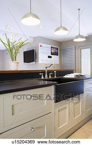 Chrome Pendant Lighting Above Cream Kitchen Unit With Black Granite Belfast Sink And Black Granite Worktop Stock Photo