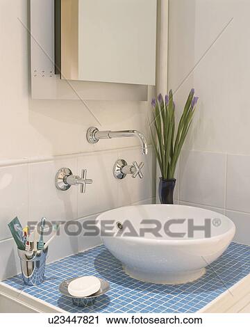 Stock Image - Chrome taps above white bowl basin on blue mosaic tiled vanity unit. Fotosearch