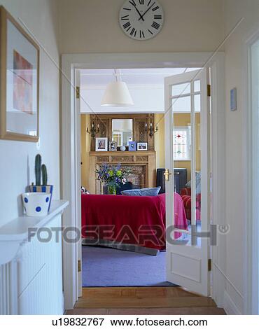 Stock Photo - Circular clock above glazed double doors open to living room with red sofa. Fotosearch