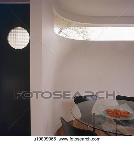 Stock Photography - Circular glass table and Arne Jacobsen Ant chairs in dining room with curved white wall. Fotosearch