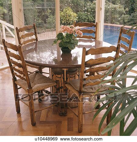 Stock Photo - Circular marble-topped table and rush-seated chairs in modern dining room. Fotosearch
