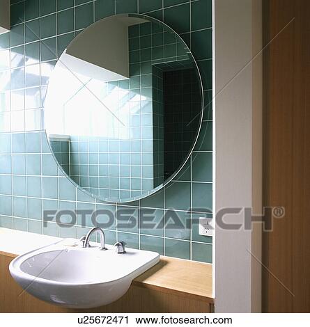 Stock Image - Circular mirror on turquoise tiled wall above fitted basin. Fotosearch