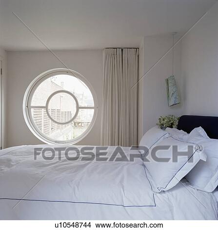 Circular window beside bed with white linen in modern white bedroom View Large Photo Image Picture - Circular window beside bed with white linen in modern white bedroom. Fotosearch
