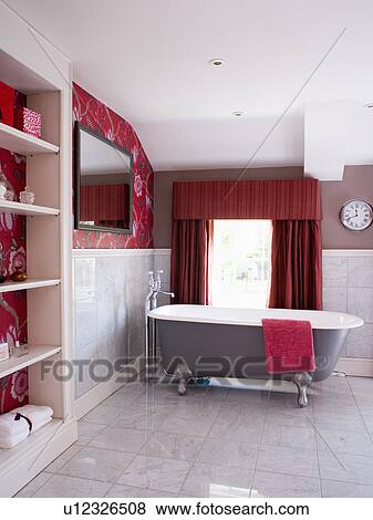 Stock Photo - Clawfoot bath in modern bathroom with red wallpaper and curtains and grey tiled flooring. Fotosearch