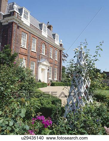 Climbing roses on white obelisk in garden in front of large Queen Anne house in the country View Large Photo Image Stock Image - Climbing roses on white obelisk in garden in front of large Queen Anne house in the country. Fotosearch