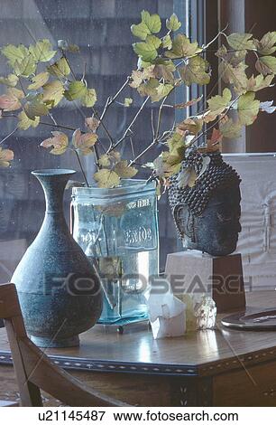 Close-up of antique pot and Thai statue on table with vase of beech leaves View Large Photo Image Stock Photo - Close-up of antique pot and Thai statue on table with vase of beech leaves. Fotosearch