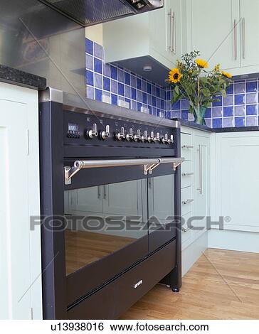 Stock Photograph - Close-up of black range oven in modern kitchen with blue ceramic wall tiles. Fotosearch