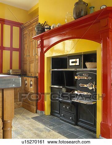 Stock Image - Close-up of black retro oven in red fireplace in yellow kitchen. Fotosearch