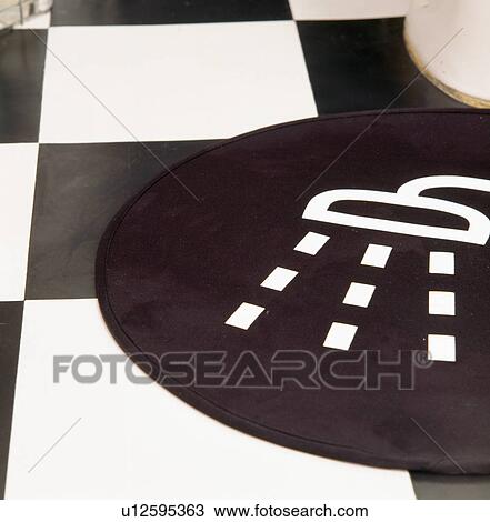 Stock Image - Close-up of black+white bathmat on black+white vinyl tiled floor. Fotosearch