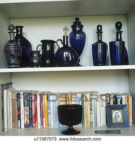 Stock Image - Close-up of blue glass decanters on shelf above books. Fotosearch