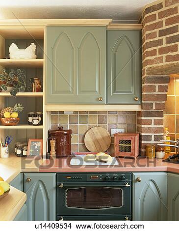 Picture - Close-up of blue-green fitted cupboard on wall of above oven in cottage kitchen. Fotosearch
