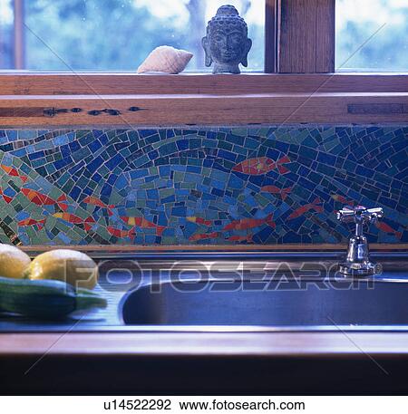 Stock Image - Close-up of blue mosaic tiled seascape above stainless steel sink. Fotosearch