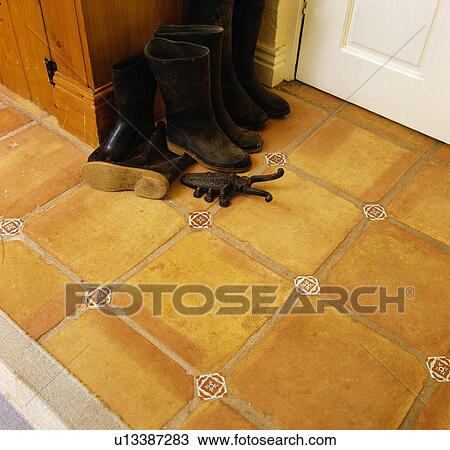Stock Image - Close-up of boots on terracotta floor tiles. Fotosearch