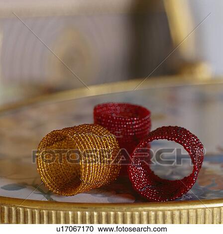 Stock Image - Close-up of bronze and red beaded table napkin rings. Fotosearch