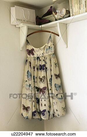 Stock Photo - Close-up of butterfly-print dress hanging from white corner shelf. Fotosearch