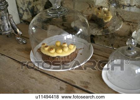 Stock Photo - Close-up of cake below glass dome on wooden table. Fotosearch
