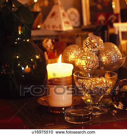 Stock Image - Close-up of candles and gold Christmas baubles on dining table. Fotosearch