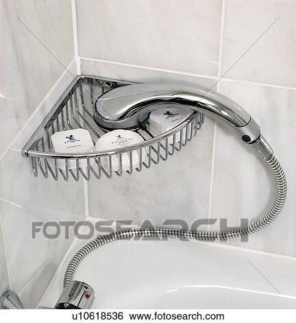 Stock Photograph - Close-up of chrome shower-spray resting on chrome corner shelf above bath. Fotosearch
