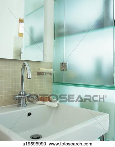Stock Image - Close-up of chrome tap and white ceramic basin in modern bathroom. Fotosearch