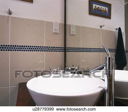 Stock Photo - Close-up of chrome tap and white circular basin in modern tiled bathroom. Fotosearch