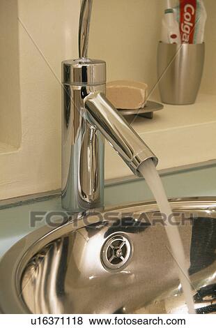 Stock Photo - Close-up of chrome tap with water pouring into stainless steel basin. Fotosearch