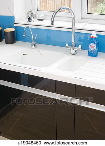 Stock Image - Close-up of chrome taps and double white sink in black fitted kitchen units. Fotosearch