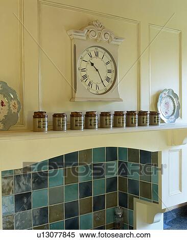Stock Photography - Close-up of clock on wall above storage jars and green Fired Earth ceramic wall tiles. Fotosearch