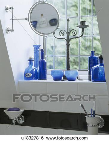 Stock Photograph - Close-up of collection of blue glass bottles with mirror on stand on windowsill. Fotosearch
