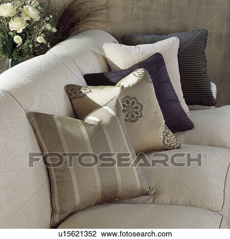 Stock Image - Close-up of cream sofa with silk striped and plain cushions. Fotosearch